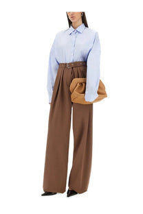 A soft tan leather structured shoulder bag with gathered top and minimalist metallic buckle shown with dries van noten brown wide leg pants