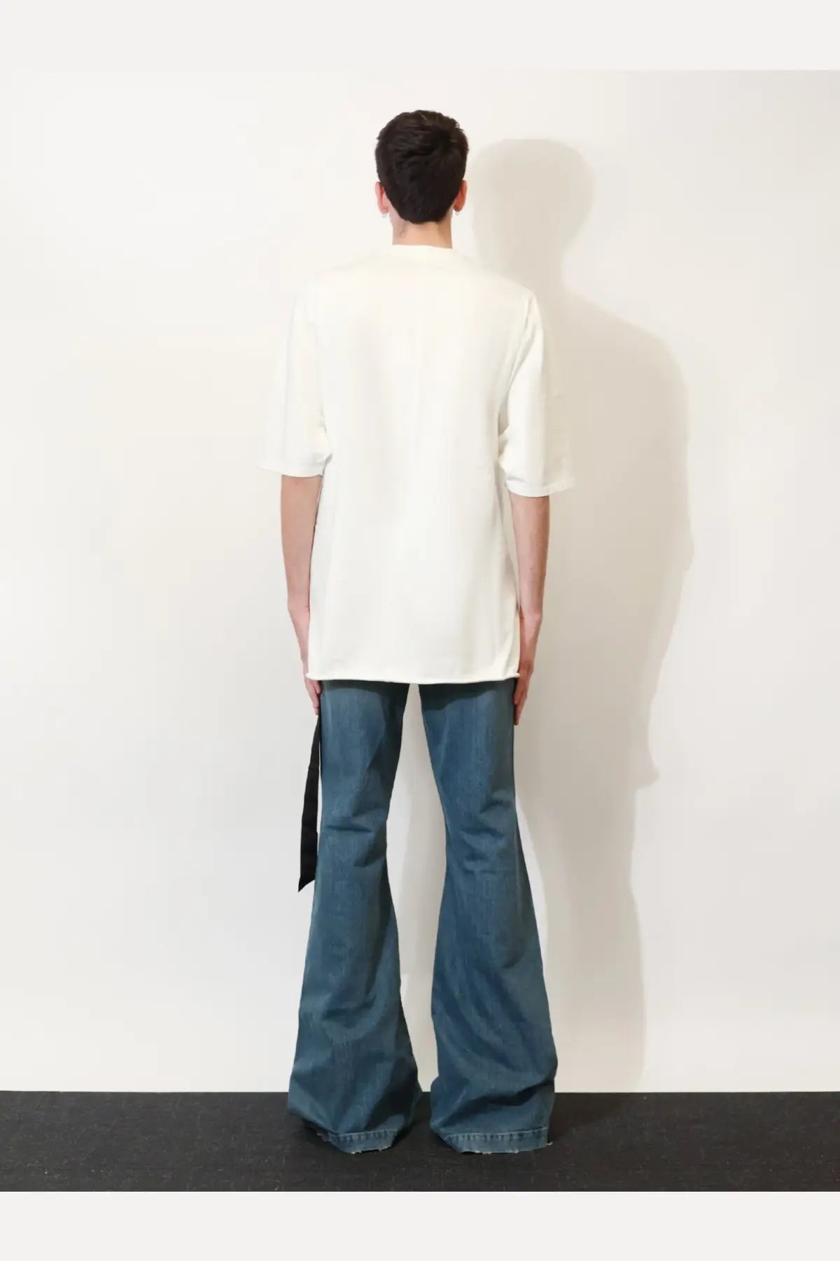 A person wearing a drkshdw men’s black cotton shirt paired with loose off-white t-shirt and dark blue flared jeans