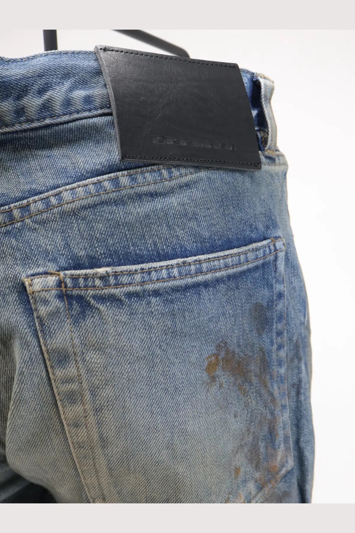 Blue denim drkshdw men’s jeans with vintage wash and black leather brand patch at the waistband back side view