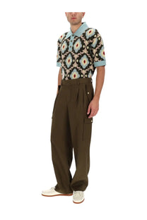 A man wearing a patterned short-sleeved polo shirt with geometric floral motifs in black beige and light blue paired with drôle de monsieur men’s brown cargo pants