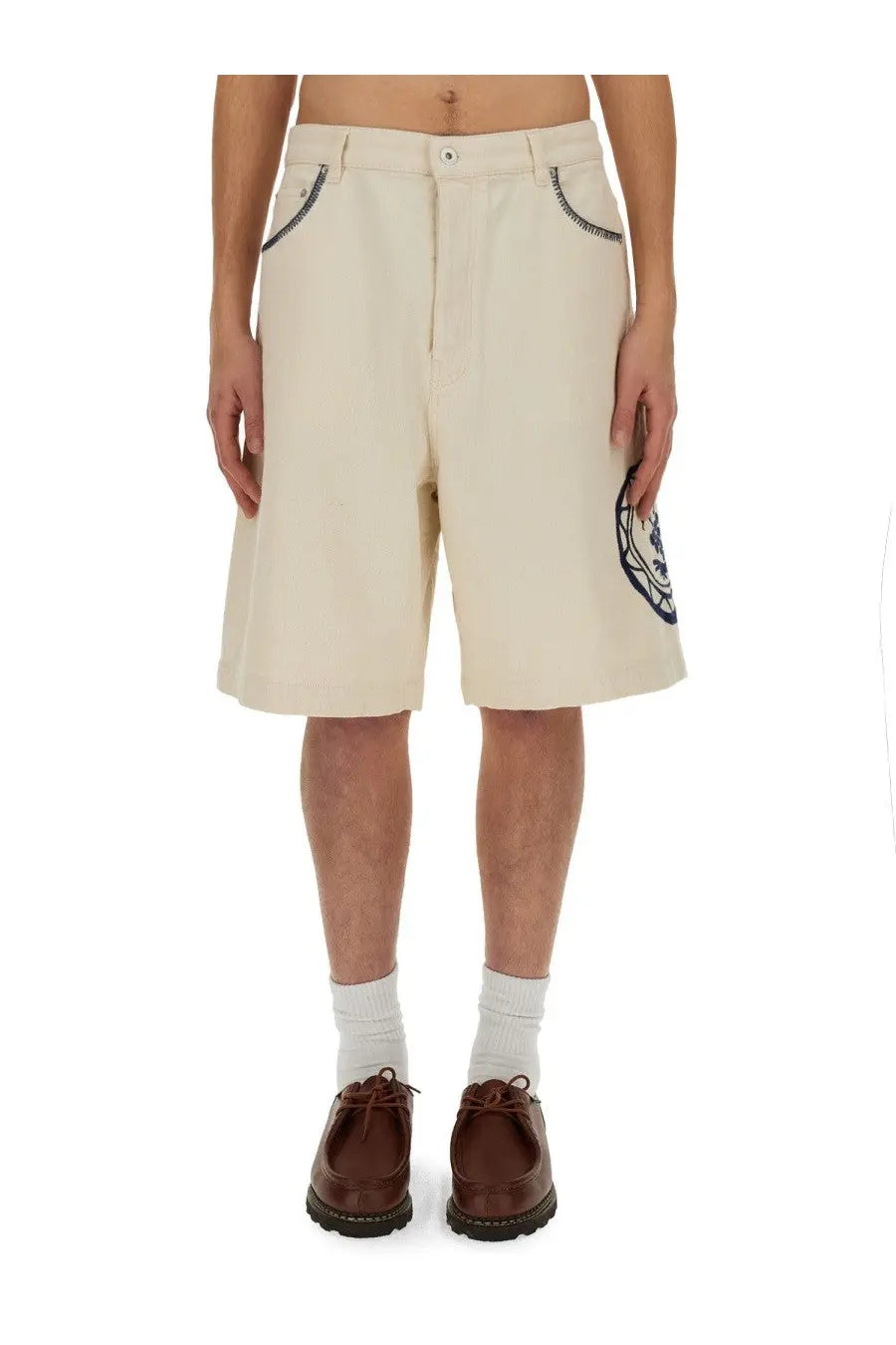 Beige Drôle de Monsieur men’s cotton bermuda shorts with black embroidered pockets and circular logo patch on leg