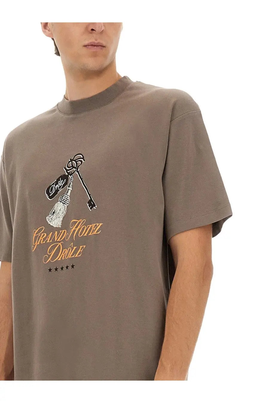 Drôle de monsieur men’s muted gray crewneck t-shirt with black and gold grand hotel drole key and broom graphic