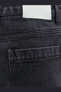 Back view of dunst men’s black denim bermuda shorts with dark-wash fabric and white leather brand label on waistband