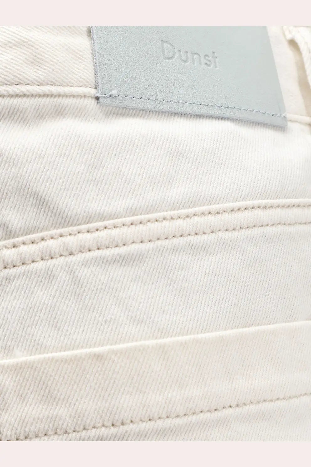 A pair of off-white denim jeans with a textured weave and light gray leather dunst brand patch on the back