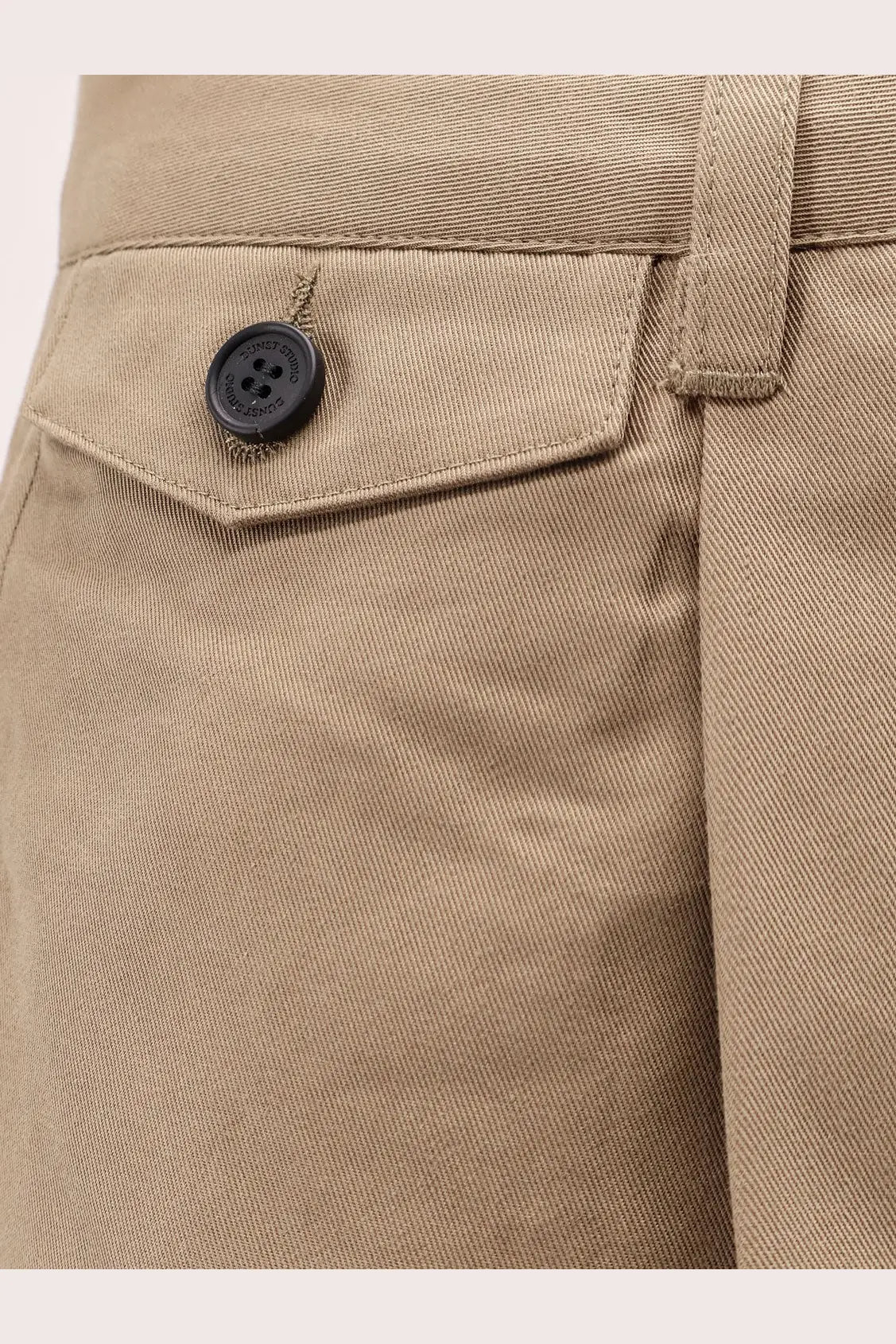 Black button with four holes on beige fabric of dunst men’s pleated brown chino slacks trousers