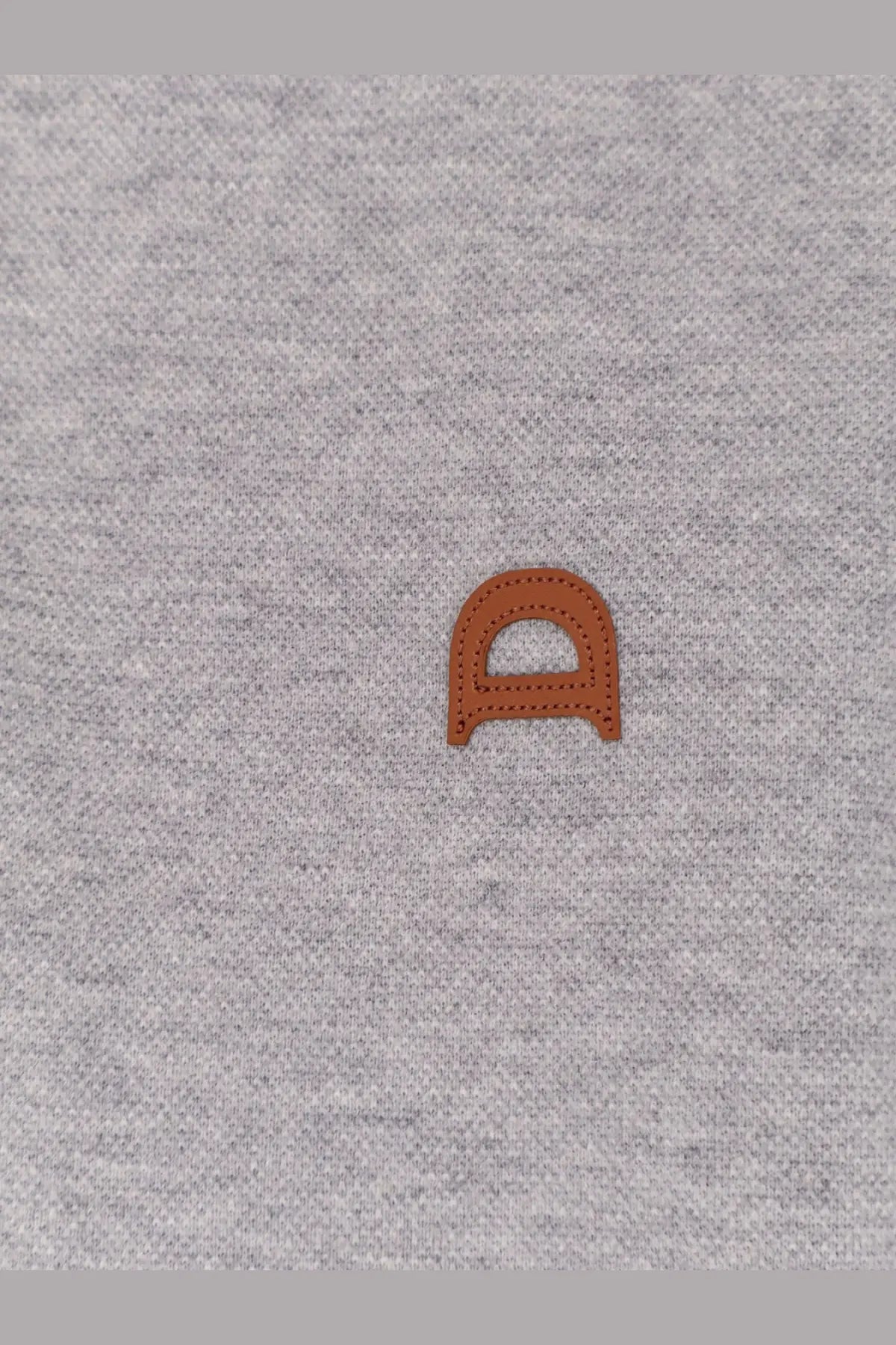 A tan leather d patch with stitched edges sewn onto heather gray fabric of dunst men’s polo shirt gray