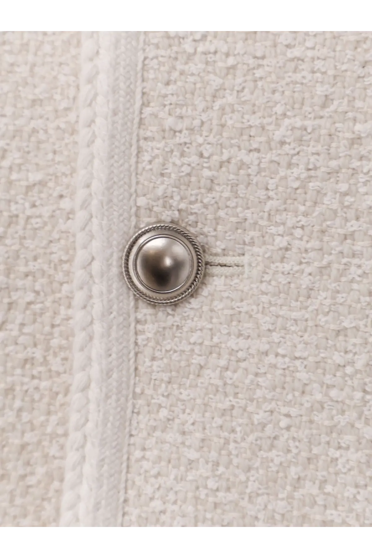 A silver-toned rope border button on the textured off-white bouclé tweed fabric of a DunSt women’s unisex blazer
