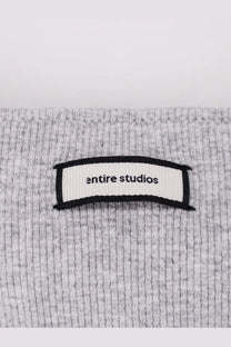 A white ribbed label with entire studios text sewn onto a heather gray textured knit fabric of a women’s ribbed cotton tank top pebble