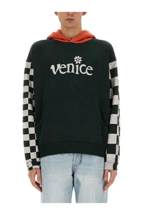 Erl men’s Venice sweatshirt in black with black and white checkered sleeves and orange hood featuring Venice logo