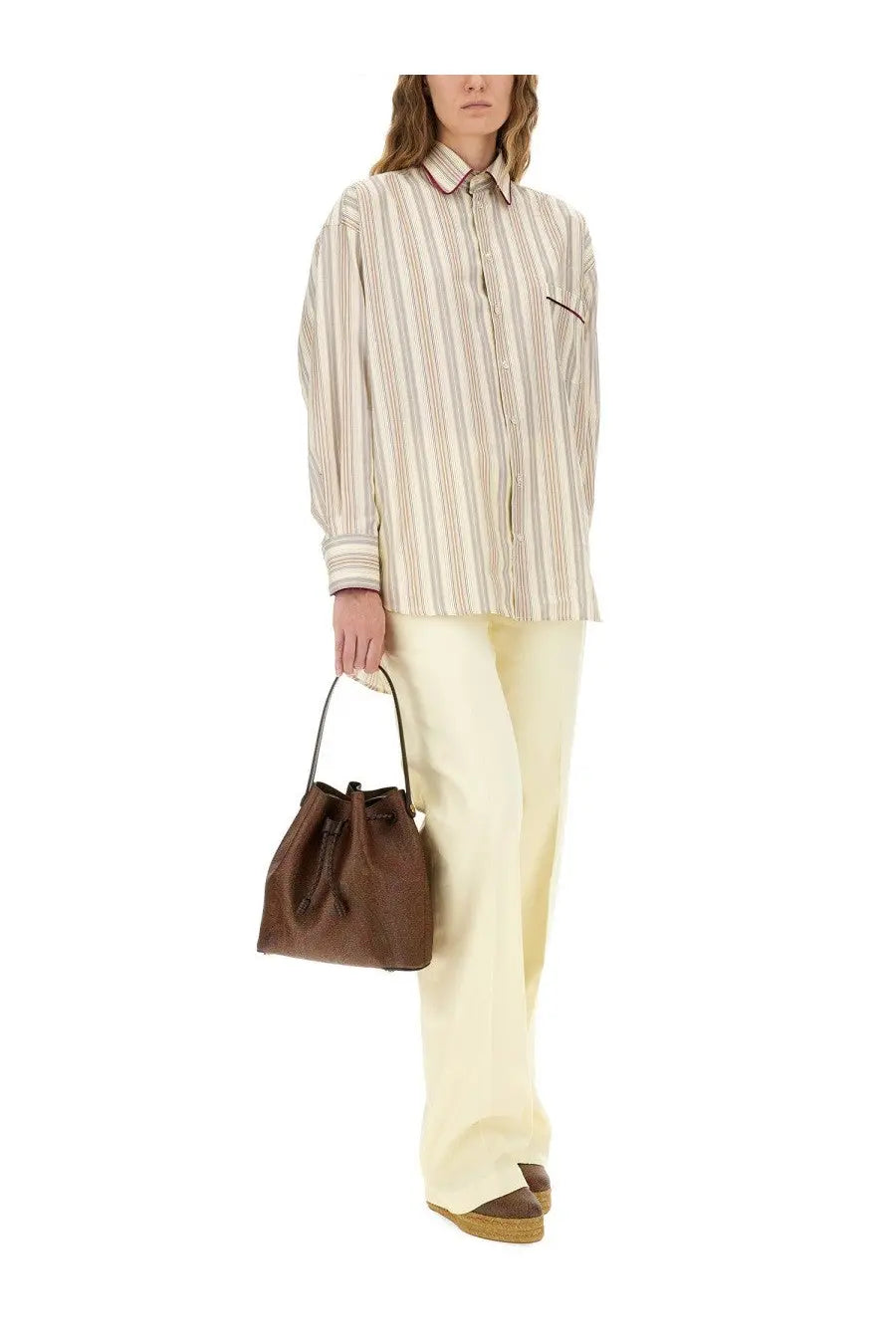 Brown leather bucket bag with drawstring closure and black handles shown with etro womens white cotton pants