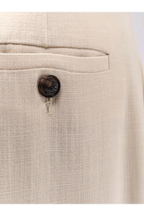 A dark circular button with embossed design on textured beige linen fabric of etro women’s white viscose trousers