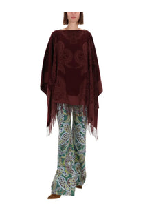 A rich burgundy velvet poncho with intricate embroidery and fringe paired with etro women’s wide blue jeans