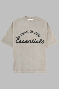 A beige oversized fear of god essentials men’s training shirt with a black logo printed across the chest