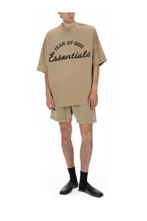 Beige oversized fear of god essentials t-shirt with black script print, paired with men’s training shorts
