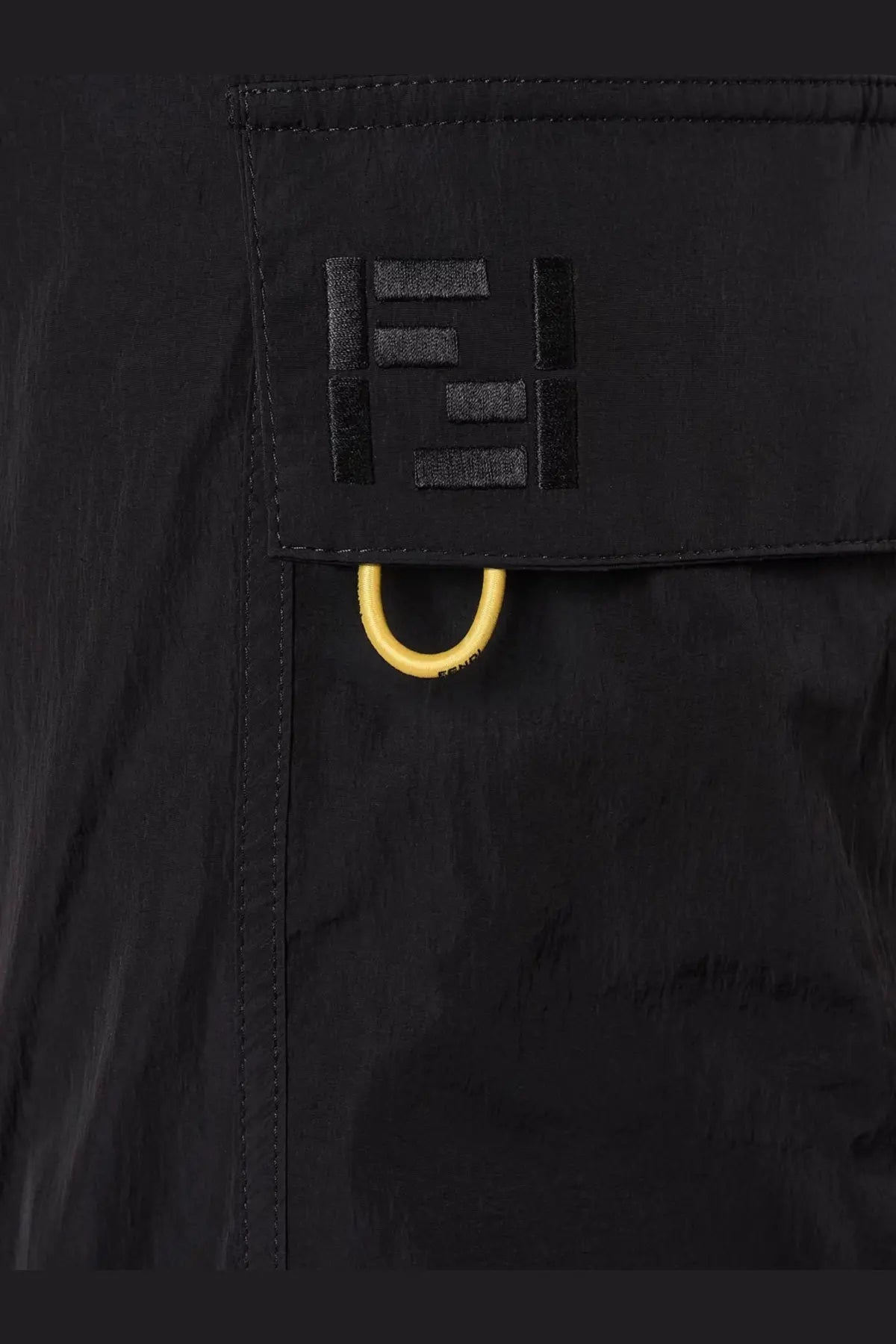 Close up of black fendi logo patch with yellow metal ring on fendi men’s cargo nylon trousers in black