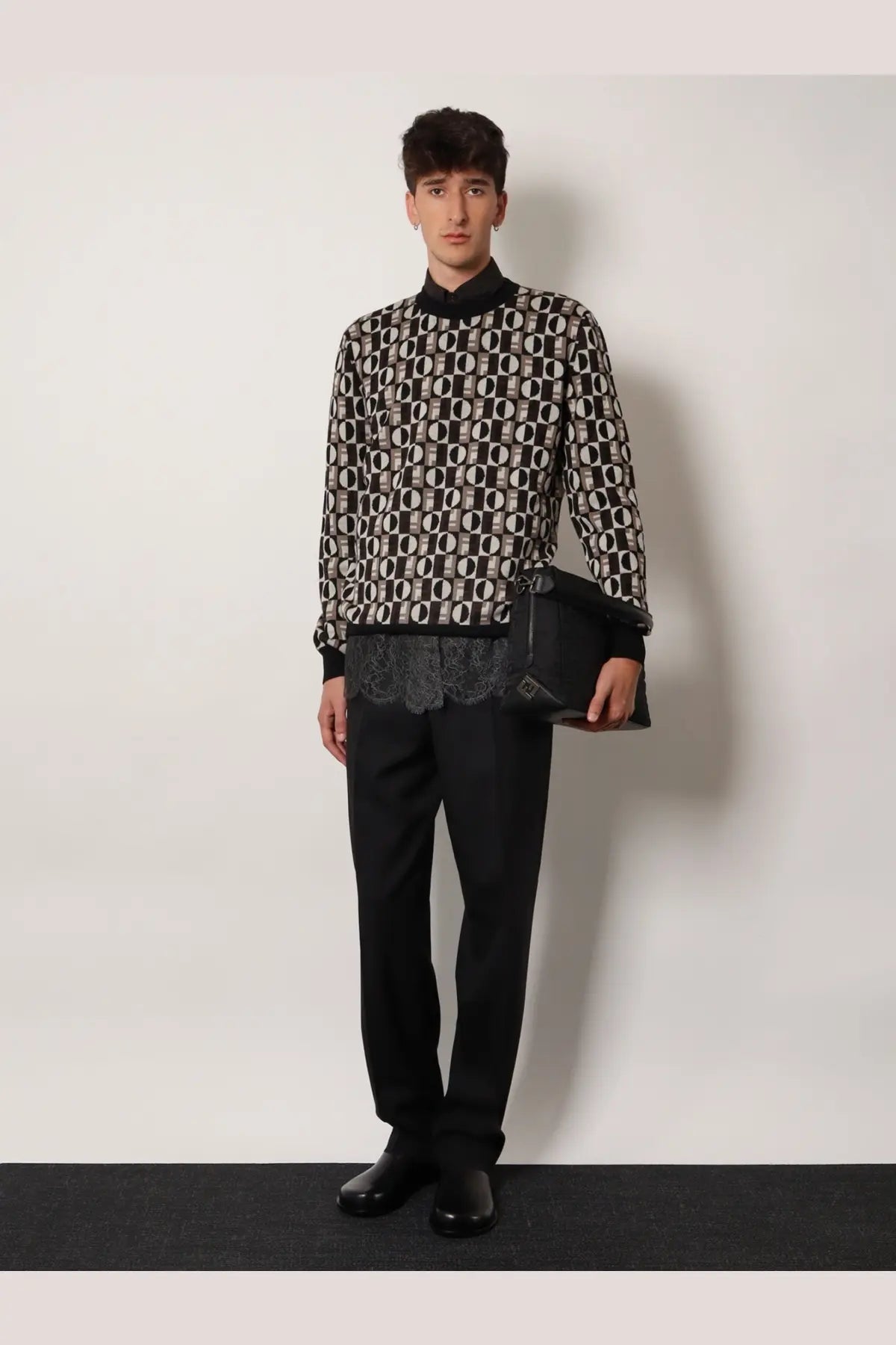 Black and white geometric patterned knit sweater with high collar paired with men’s Fendi Lui large black nylon crossbody bag
