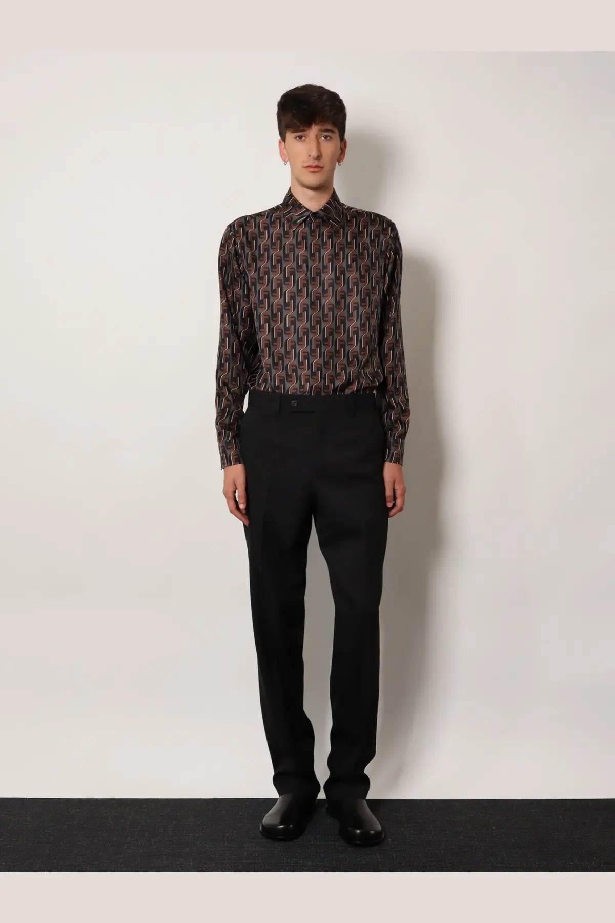 A man wearing a dark long-sleeved geometric patterned shirt paired with black Fendi men’s virgin wool trousers