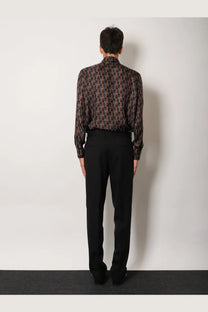 A man wearing a dark patterned long-sleeved shirt with geometric designs paired with fendi men’s virgin wool black trousers