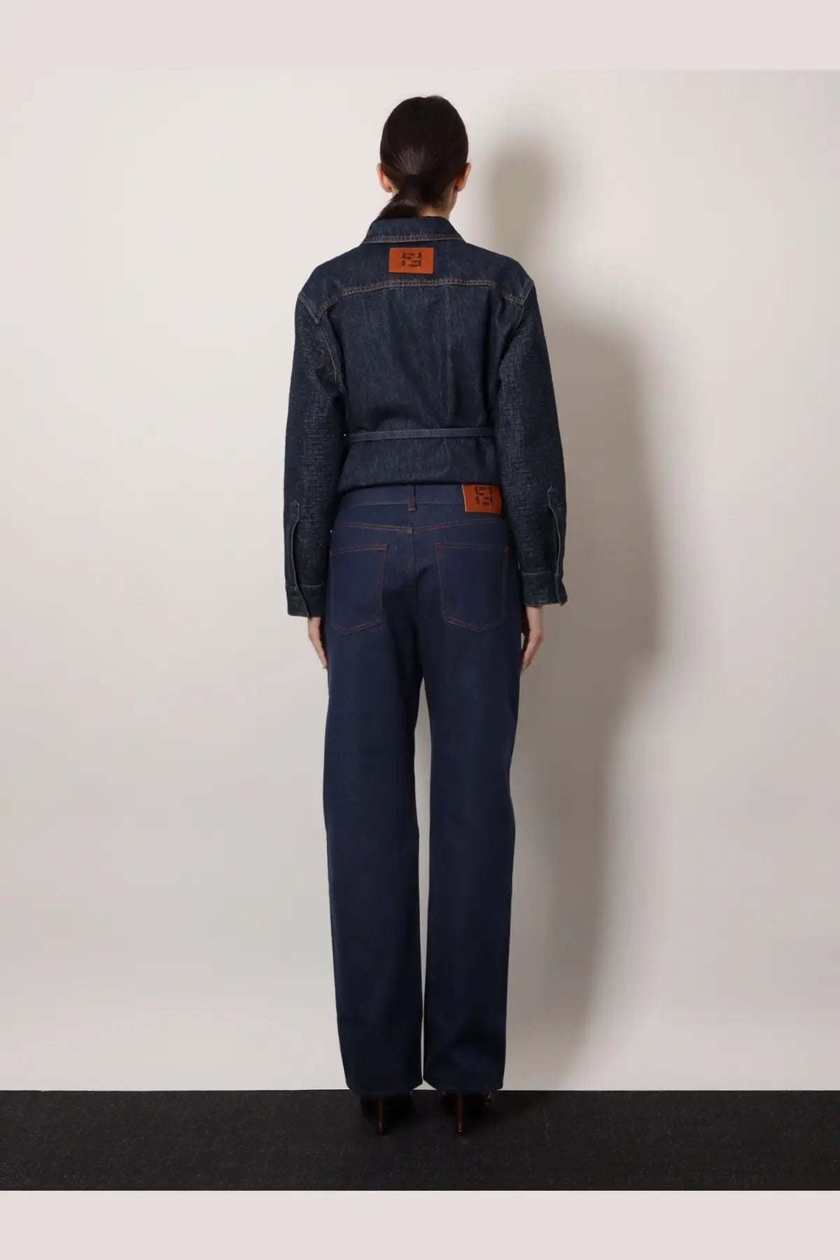 Back view of fendi women’s blue dark denim jumpsuit with brown leather patches on back and waistband