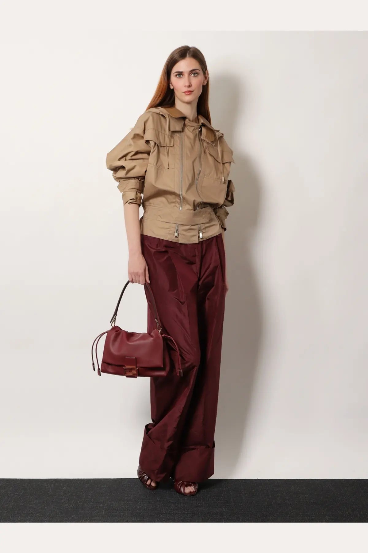 A structured burgundy leather handbag with top handle and adjustable shoulder strap shown with fendi women’s beige cotton jacket