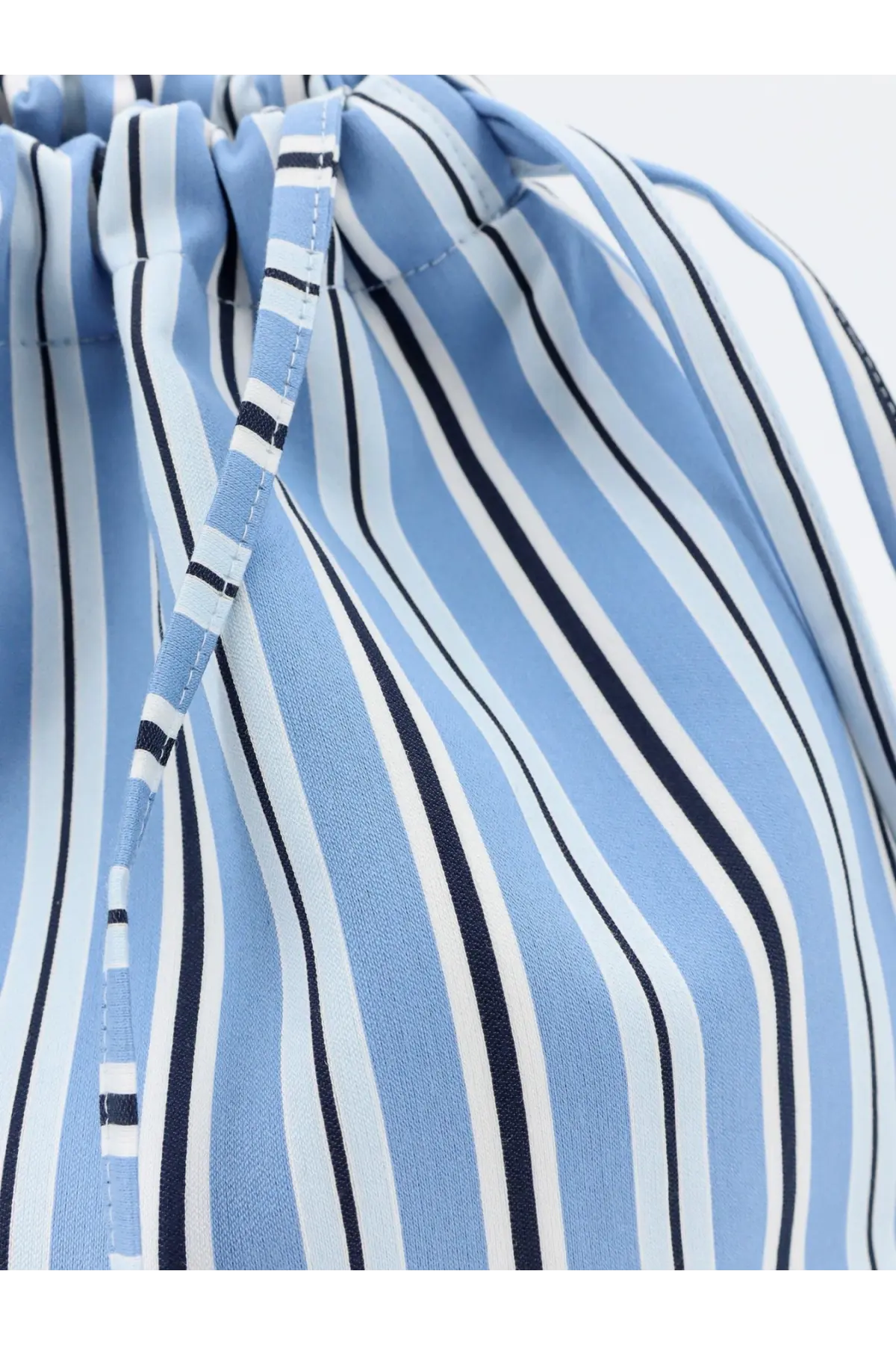 The Frankie Shop women’s Morgan Pochette is a light blue and white striped drawstring bag with navy fabric cord closure
