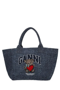 Denim-textured ganni trapeze tote bag in blue with an embroidered teddy bear holding a red heart and arched brand name