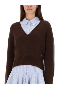 Ganni women’s brown v-neck knit sweater worn over a light blue and white striped button-down shirt