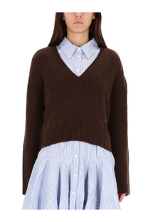Ganni women’s brown v-neck knit sweater layered over a light blue and white striped button-up shirt