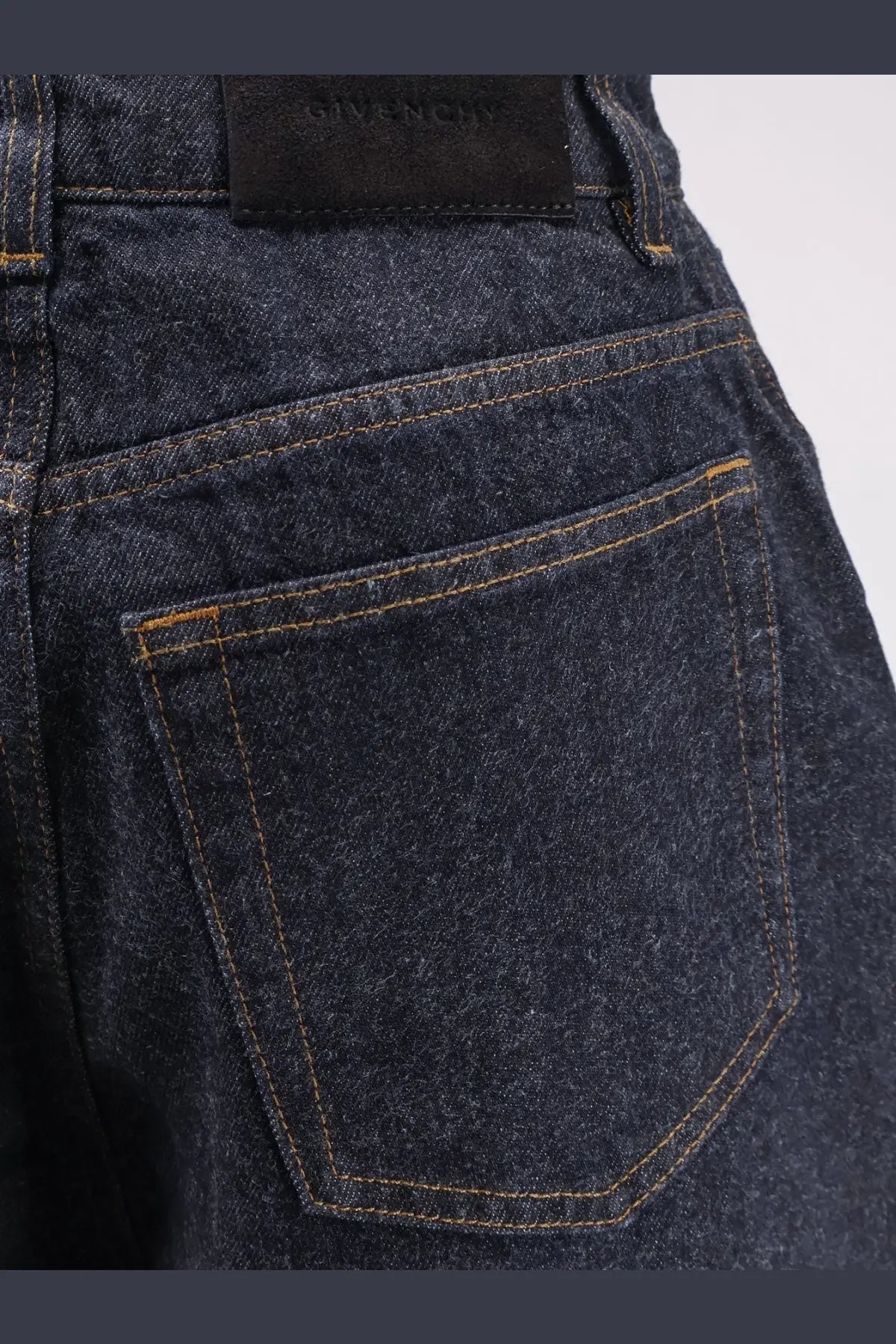 Givenchy women’s twisted dark blue denim jeans with tan stitching and black brand label at the waistband