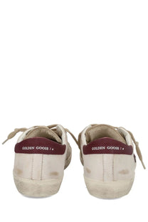 Cream-colored suede Golden Goose men’s Superstar sneakers with distressed look and maroon heel tabs with logo visible from back