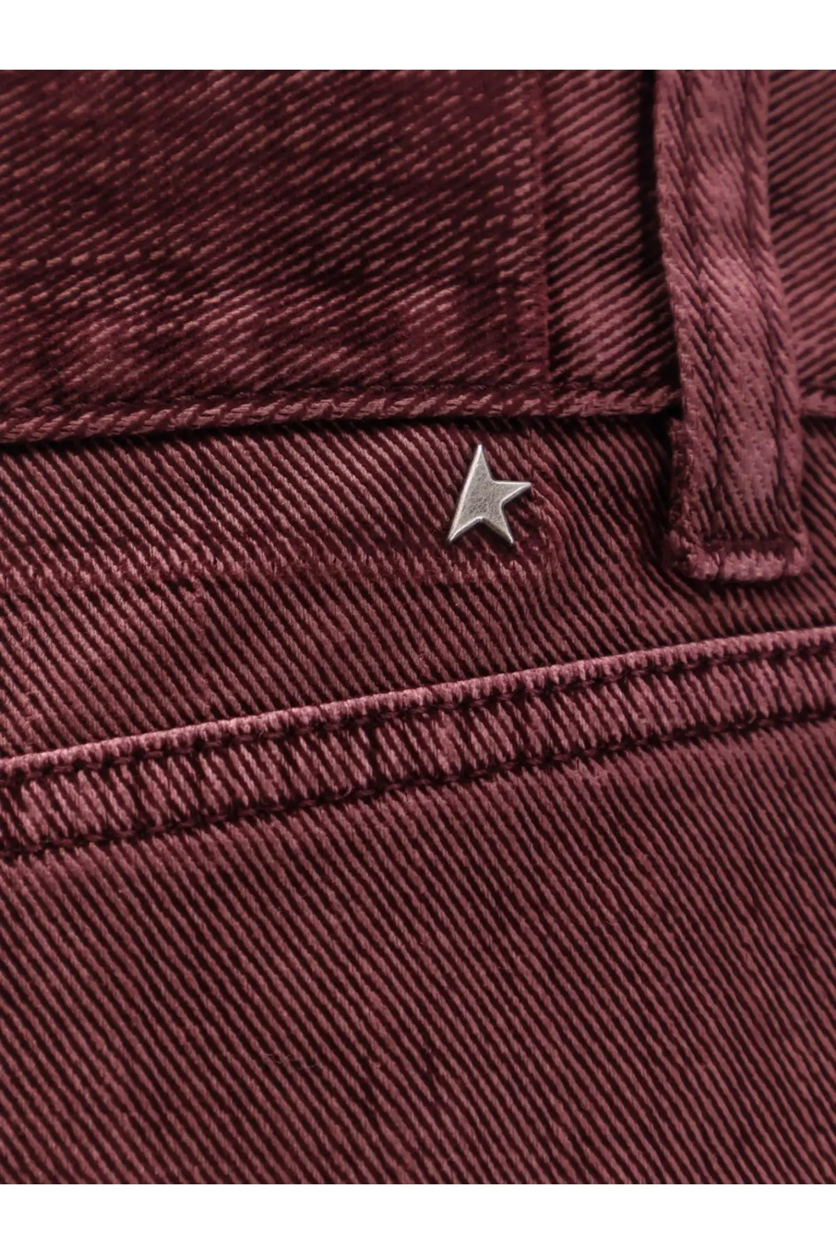 A small metallic star-shaped logo pin on maroon corduroy pants contrasting golden goose womens trousers