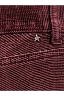 A small metallic star-shaped logo pin on maroon corduroy pants contrasting golden goose womens trousers