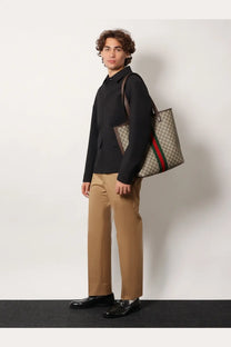 Beige and brown gucci gg supreme tote bag with red and green striped side stripe paired with gucci men’s cotton trousers beige