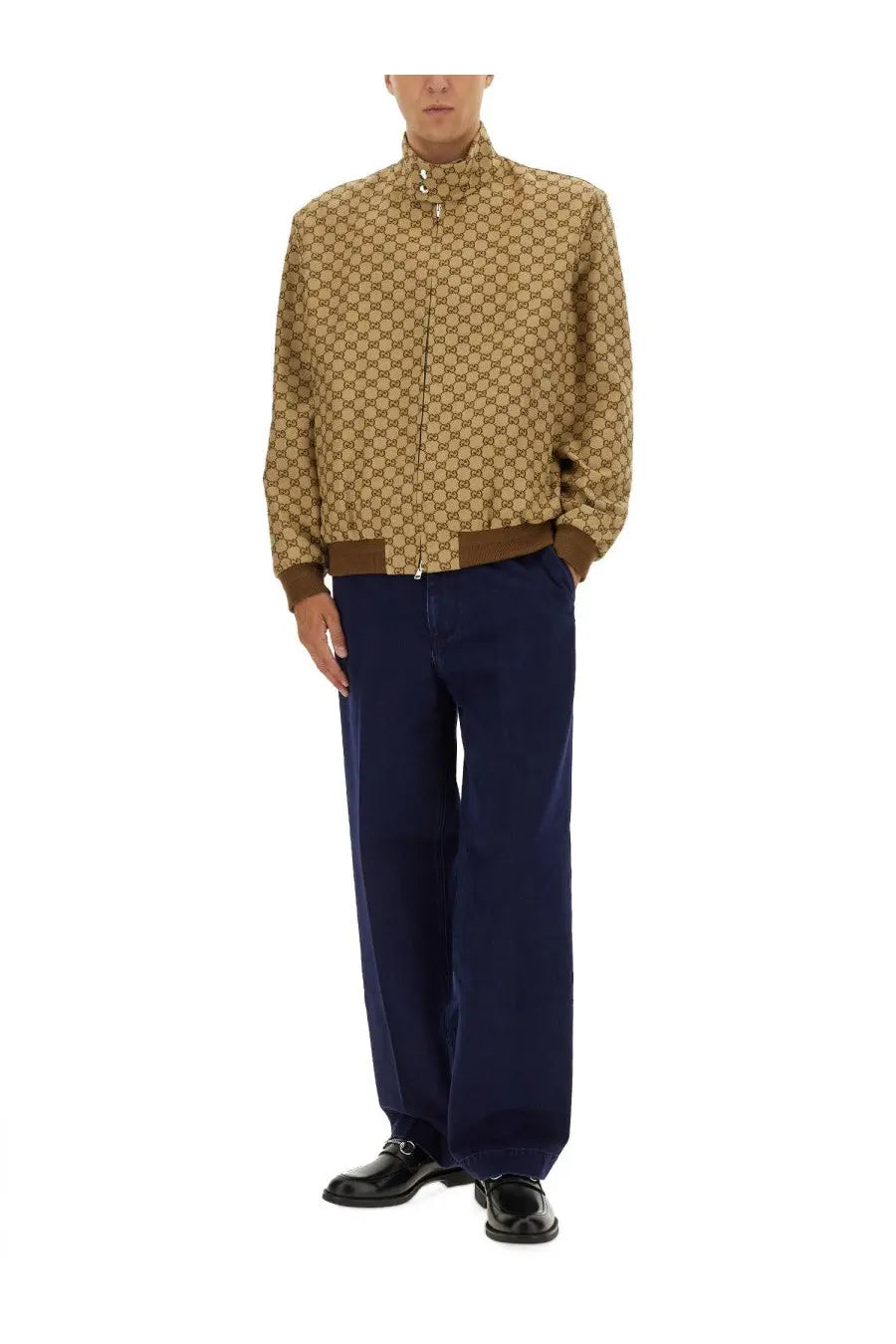 Beige gucci bomber jacket with brown trim and repeating gg logo pattern paired with blue élavé denim pants