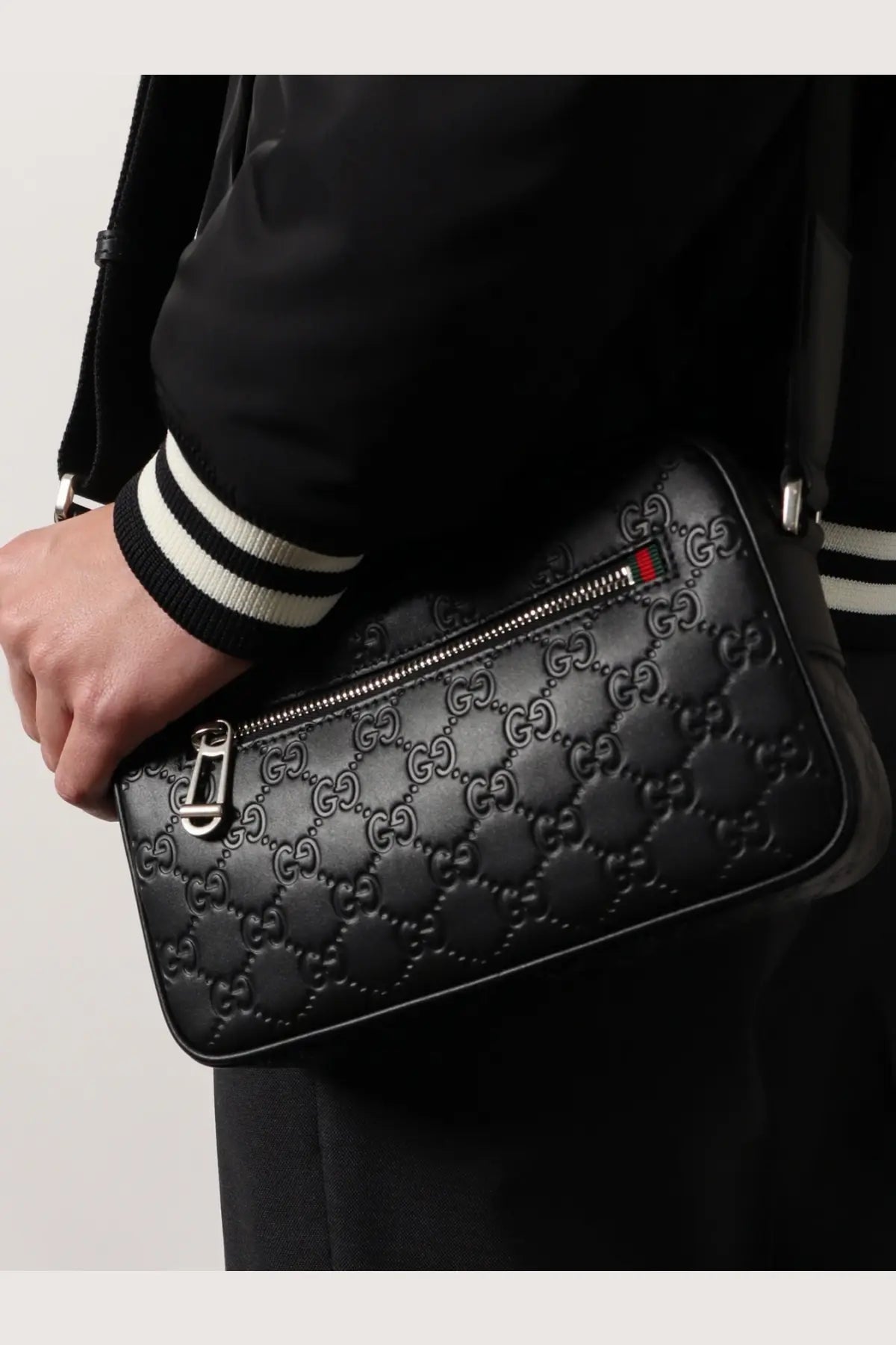 Black gucci men’s gg emblem embossed leather crossbody bag with silver hardware and red blue zipper pull