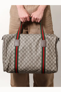 Beige Gucci men’s GG supreme canvas duffel bag with red and green striped handles for travel use