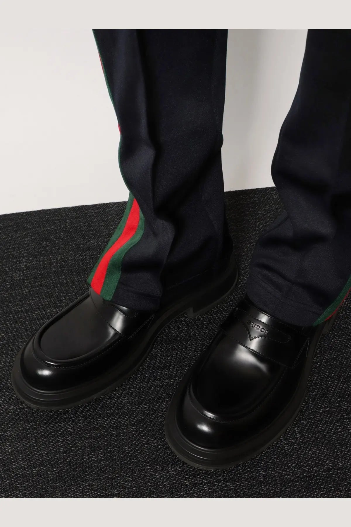 Black leather Gucci men’s loafers with glossy finish and signature red and green striped web detail on the side
