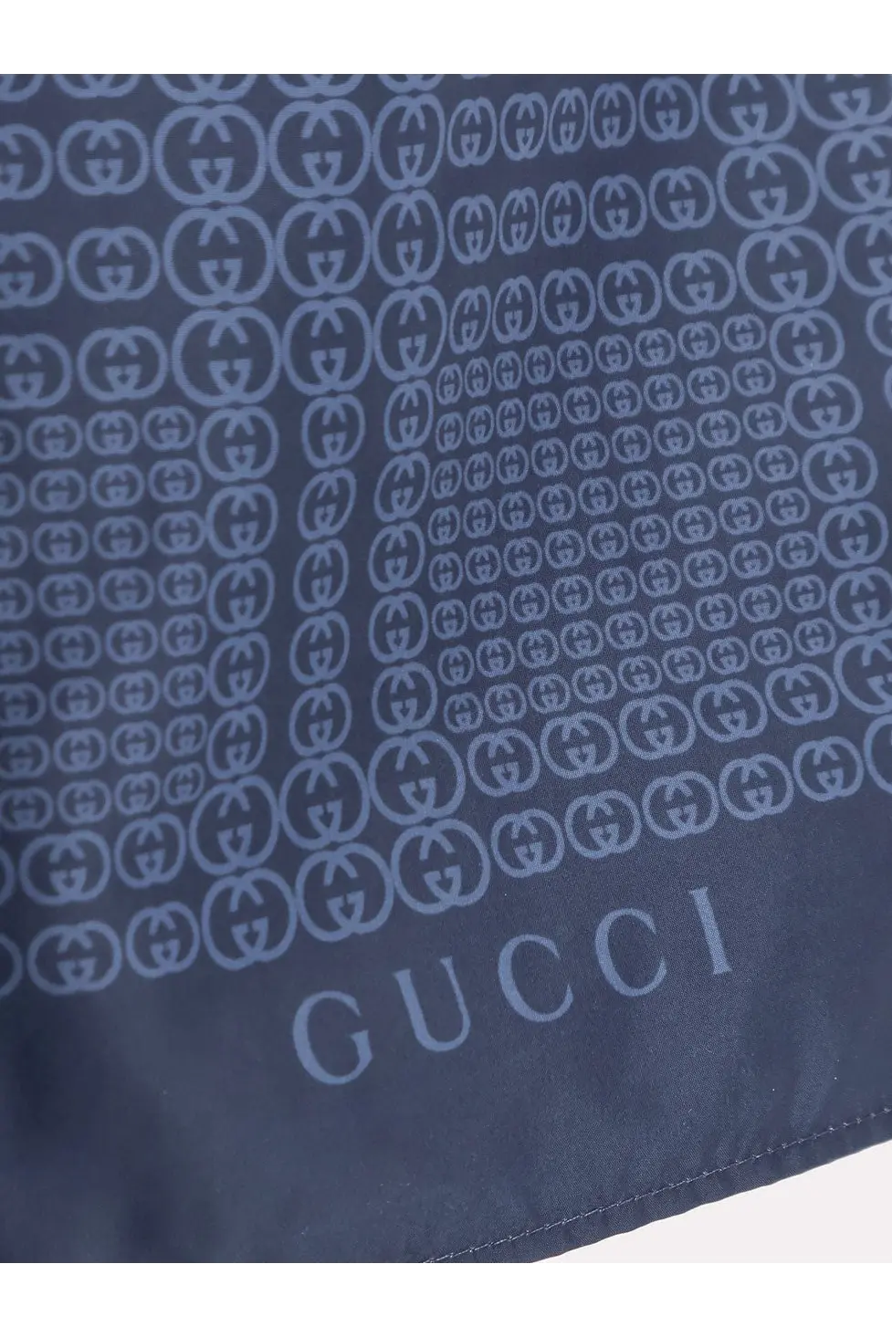 Dark blue Gucci silk scarf with repeating interlocking G logo pattern in lighter blue paired with men’s nylon swim trunks