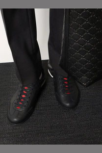 Black leather Gucci men’s sneakers with red laces and a white side stripe for stylish casual wear