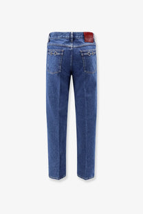 Back side of gucci men’s slim blue denim jeans with red leather brand patch and metallic ring details on pockets