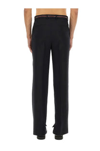 Black tailored wool trousers with slim fit and subtle pleats featuring a red and white branded belt at waistband