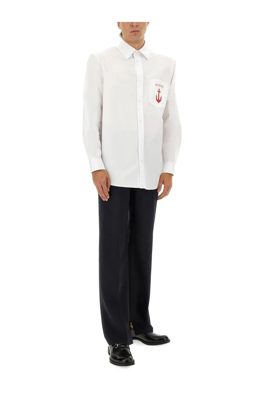 White gucci men’s long-sleeved button-down shirt with red anchor logo on chest pocket paired with blue wool pants