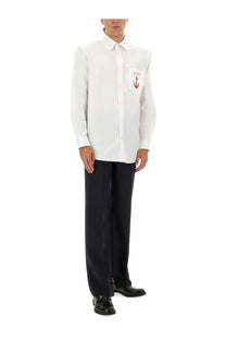 White gucci men’s long-sleeved button-down shirt with red anchor logo on chest pocket paired with blue wool pants
