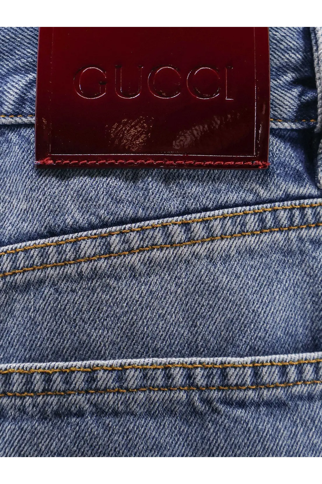 A burgundy leather gucci label stitched on the back of blue denim gucci womens cotton jeans