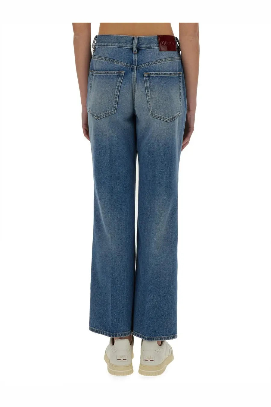 Blue denim jeans with a faded wash wide-leg cut and a red leather gucci brand patch at the waistband