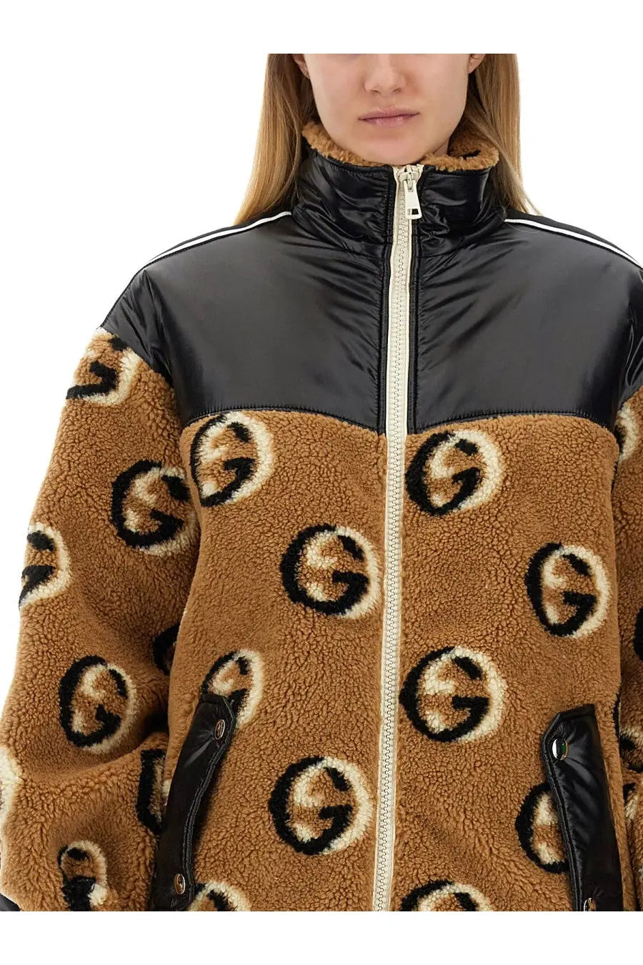 Gucci women’s beige jacquard zipper jacket with tan shearling, black and white logo pattern, and glossy black nylon shoulders
