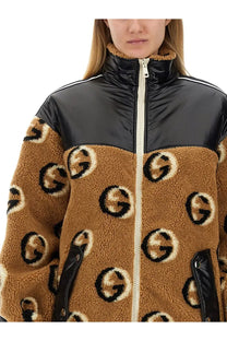 Gucci women’s beige jacquard zipper jacket with tan shearling, black and white logo pattern, and glossy black nylon shoulders