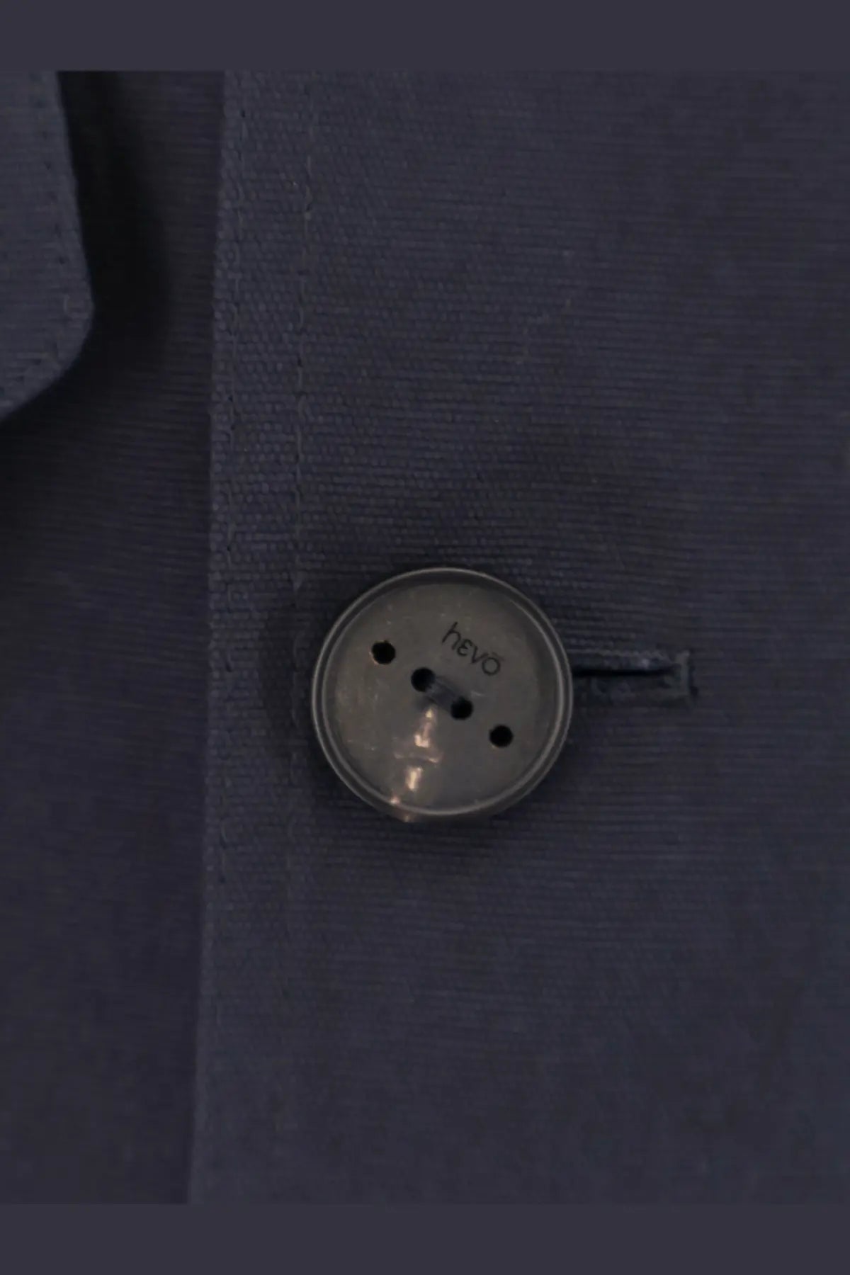 A silver-toned round button with four holes and hevò brand name on a blue cotton hevò men’s isola di san pietro jacket