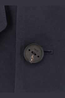A silver-toned round button with four holes and hevò brand name on a blue cotton hevò men’s isola di san pietro jacket