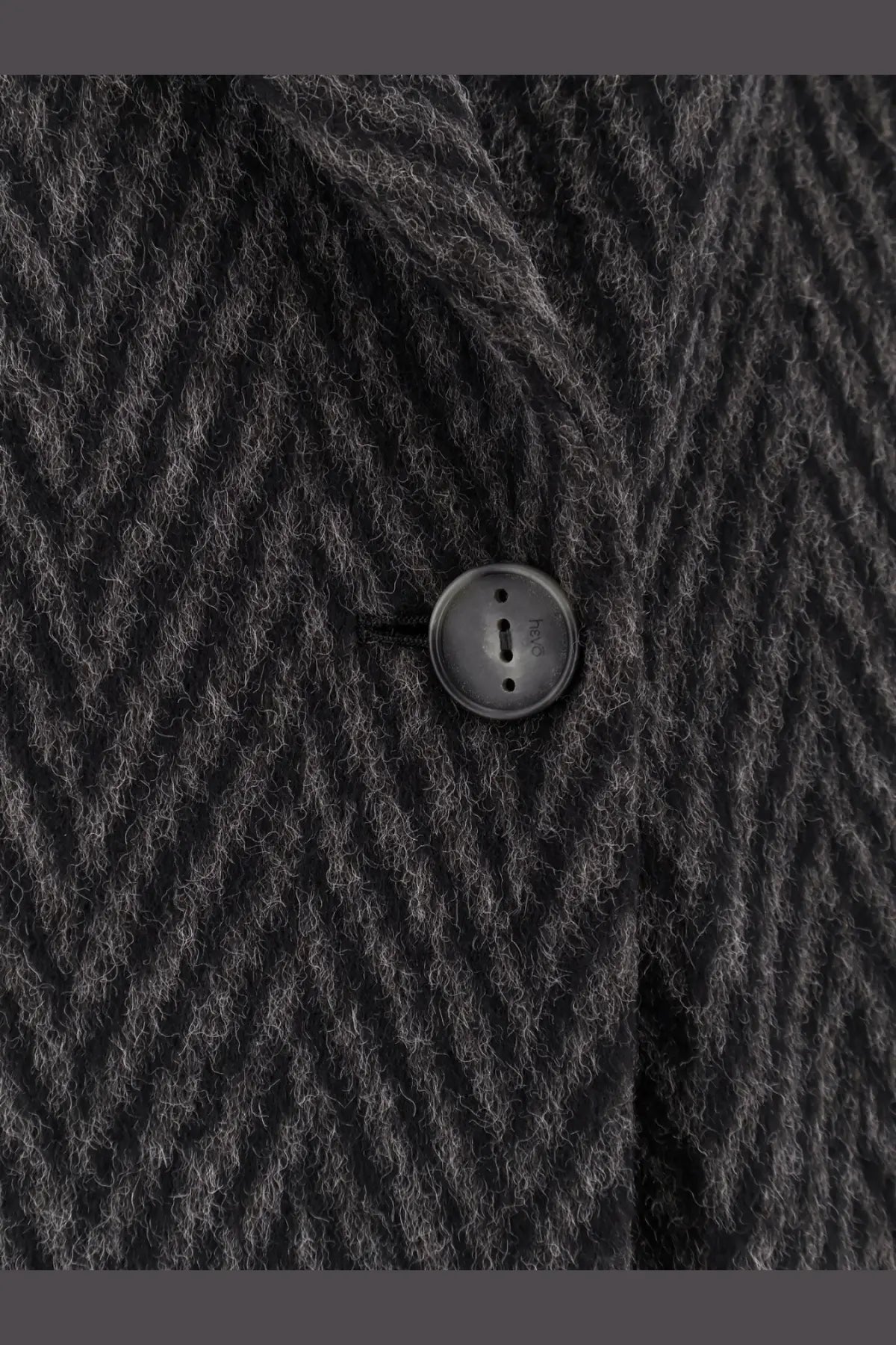 Black circular matte button embedded in dark gray herringbone wool fabric on hevò men’s santa cesarea coat